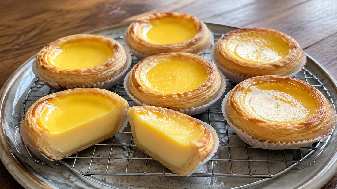 Flaky Cantonese egg tarts with glossy yellow custard and one cut open to show layered pastry