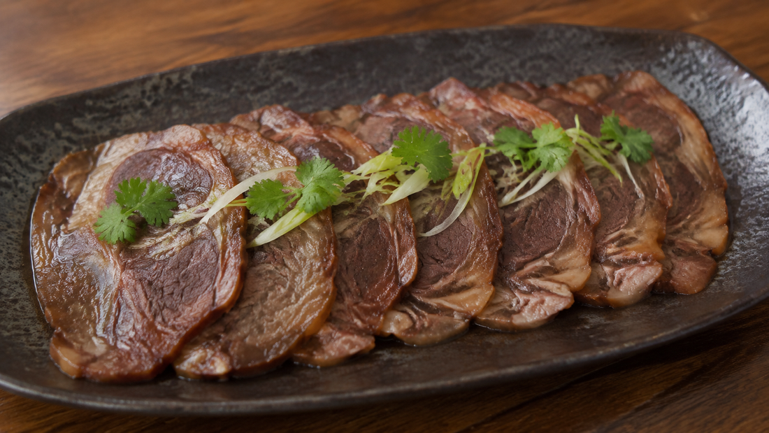 Thin slices of Chinese soy-braised beef shank with visible tendon marbling, cilantro and scallion