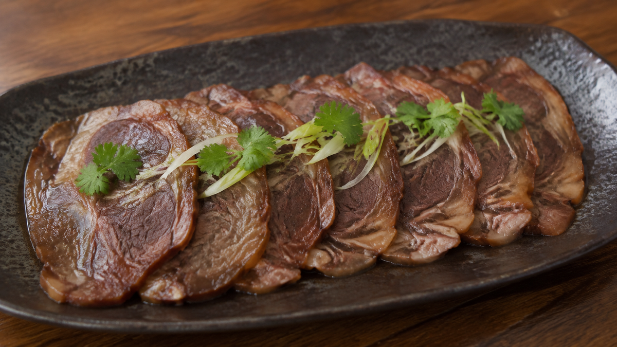 Thin slices of Chinese soy-braised beef shank with visible tendon marbling, cilantro and scallion