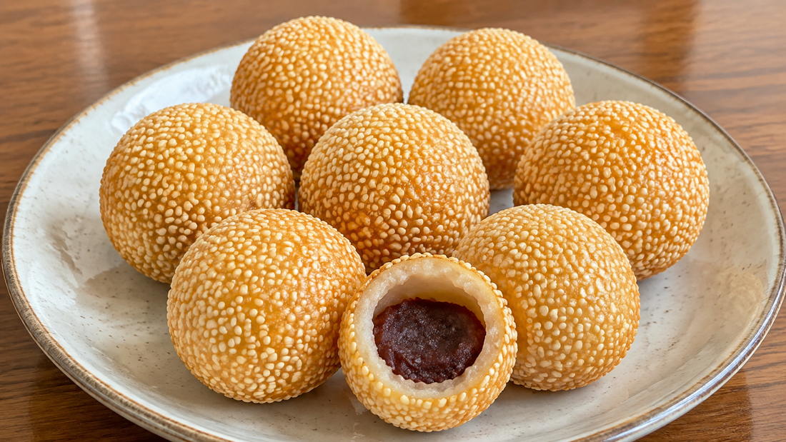Golden Chinese sesame balls with one cut open to show a hollow chewy shell and red bean paste